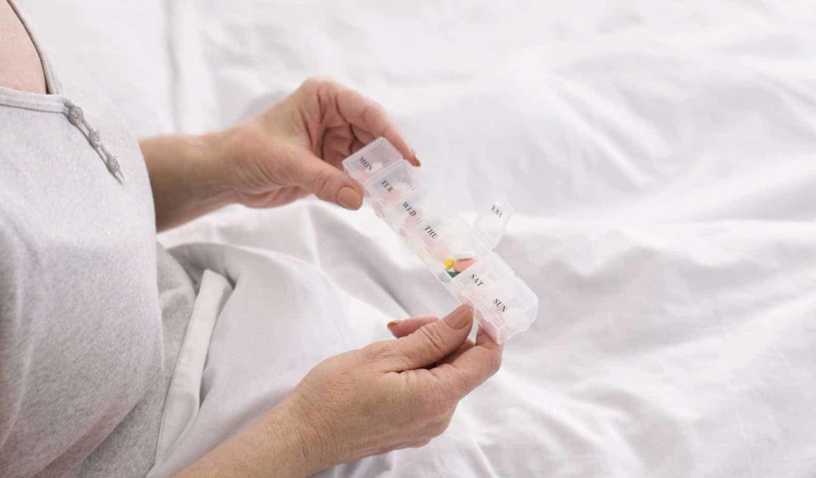 Senior woman taking medication from pill box in bed