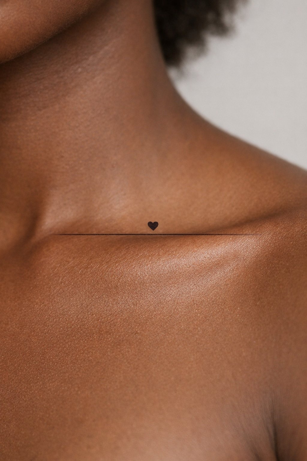 Extreme close-up of a black girl collarbone area: a thin, straight horizon line tattoo with a micro solid heart floating above it. The skin is unadorned, with the tattoo positioned like a tiny, personal landmark. The tattoo should be realistic.