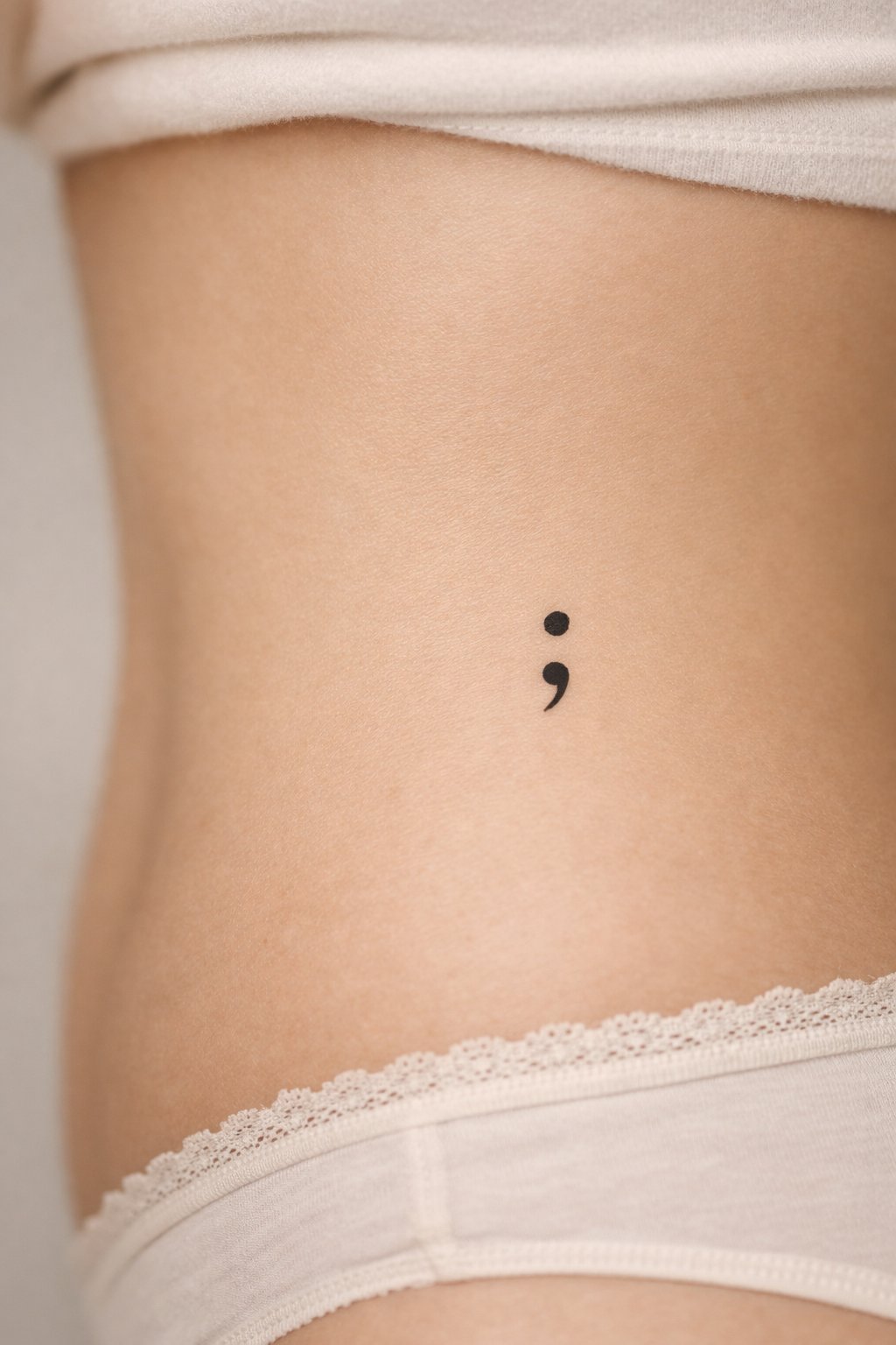 Intimate close-up on the side waist: a thin, precise semicolon tattoo. The lighting is soft and respectful, with a focus on the symbol's clean lines."