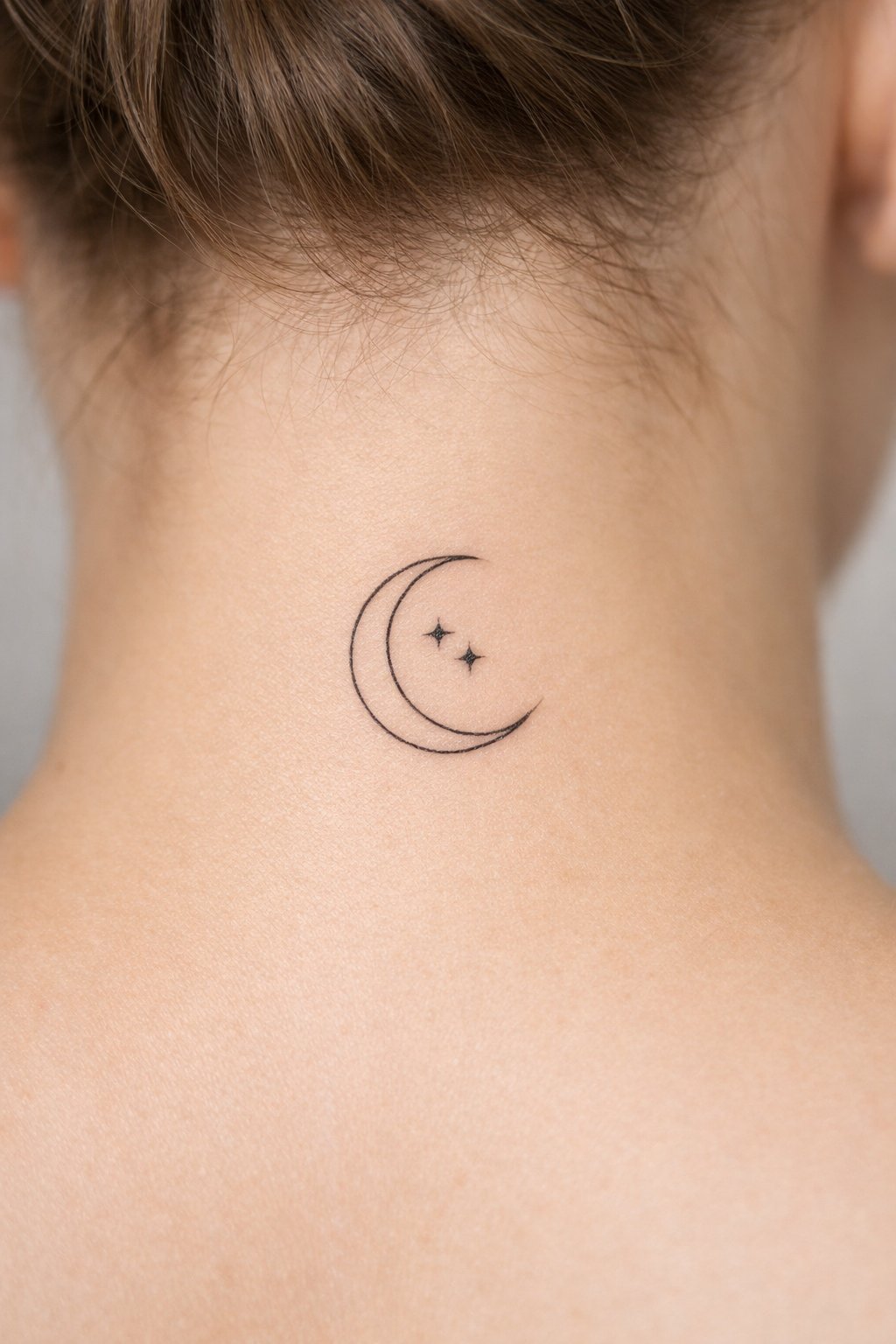 Nape of the neck detail: a crescent moon with two micro stars inside its curve. Fine linework, with the moon's points sharp and delicate.