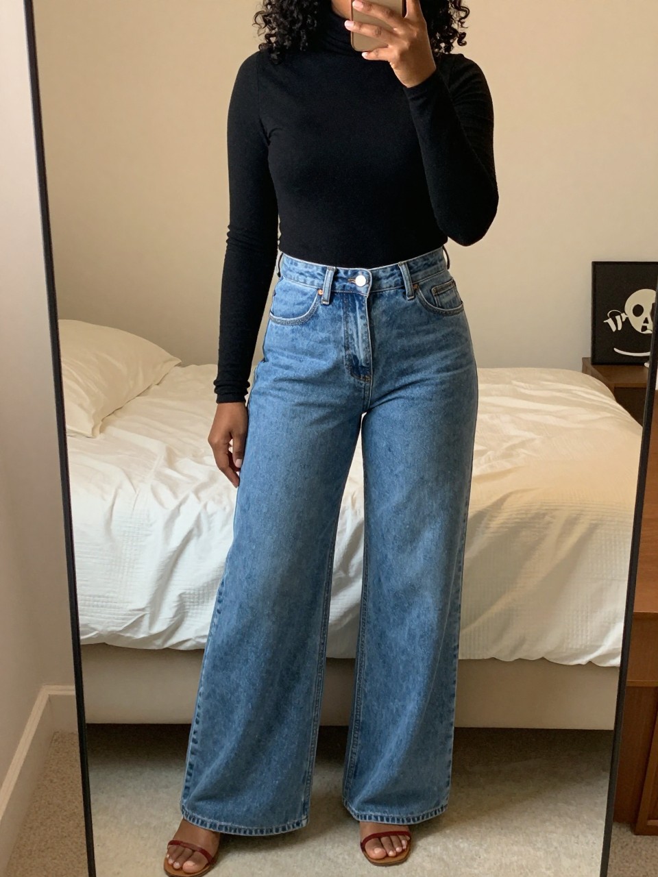 iPhone mirror selfie of a black woman in wide-leg jeans and turtleneck with Timbs, hand in pocket, cropped at NECK so face doesn't show, in a feminine-themed bedroom with warm moody lighting, iPhone photo quality.
