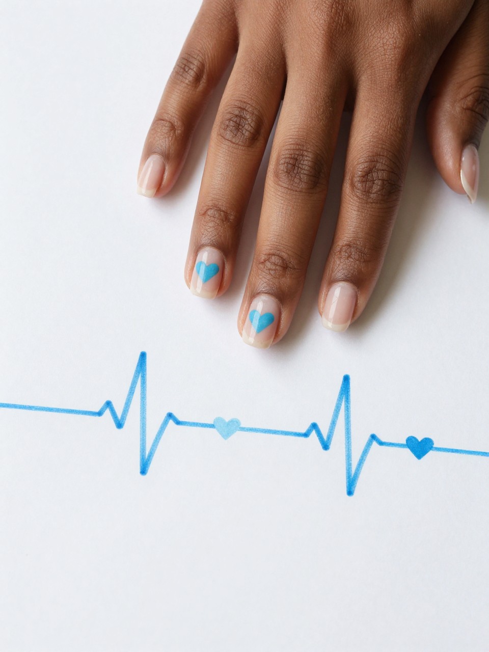 Overhead view of black feminine hand with pristine natural nails on a white sheet of paper. Each nail design has a single sky blue heartbeat line that ends in a small heart. The aesthetic is clean, modern, and full of quiet sentiment.