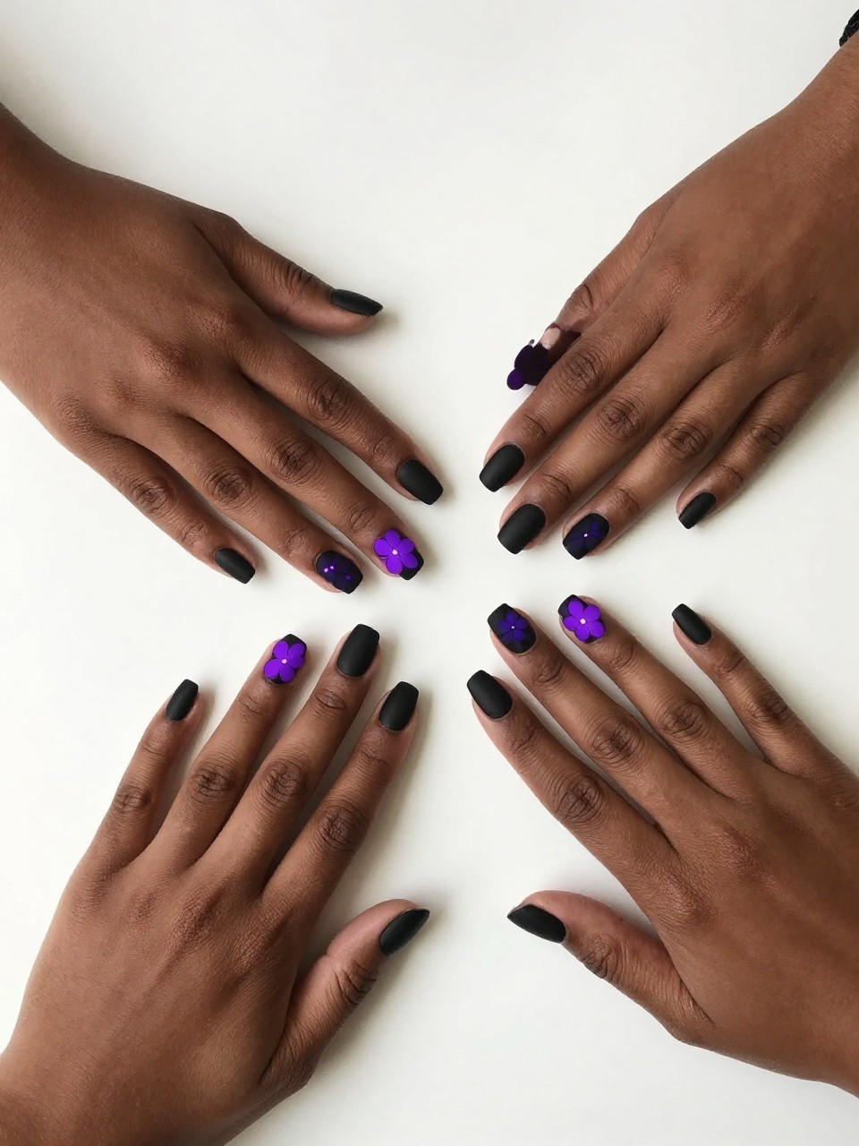 Overhead view of black feminine hands in a bright room. The nails are matte black. Simple floral shapes are painted in a bright, almost glowing purple. The mood is club-ready and modern.