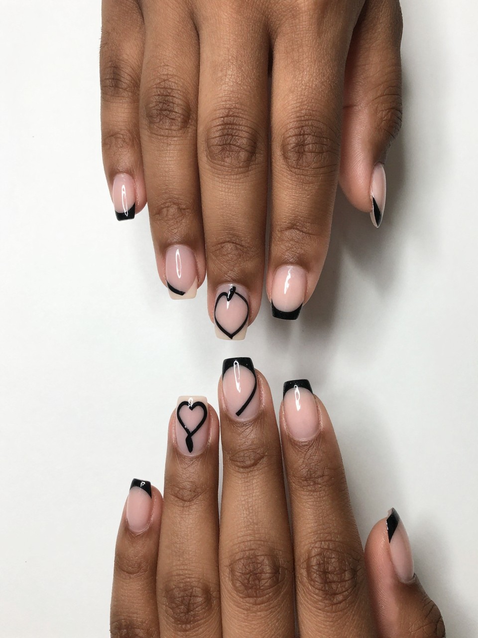 Overhead view of black feminine hands with a diagonal black French tip on each nail. At the end of the diagonal line on each nail design, the line curves to form an open, asymmetric heart
