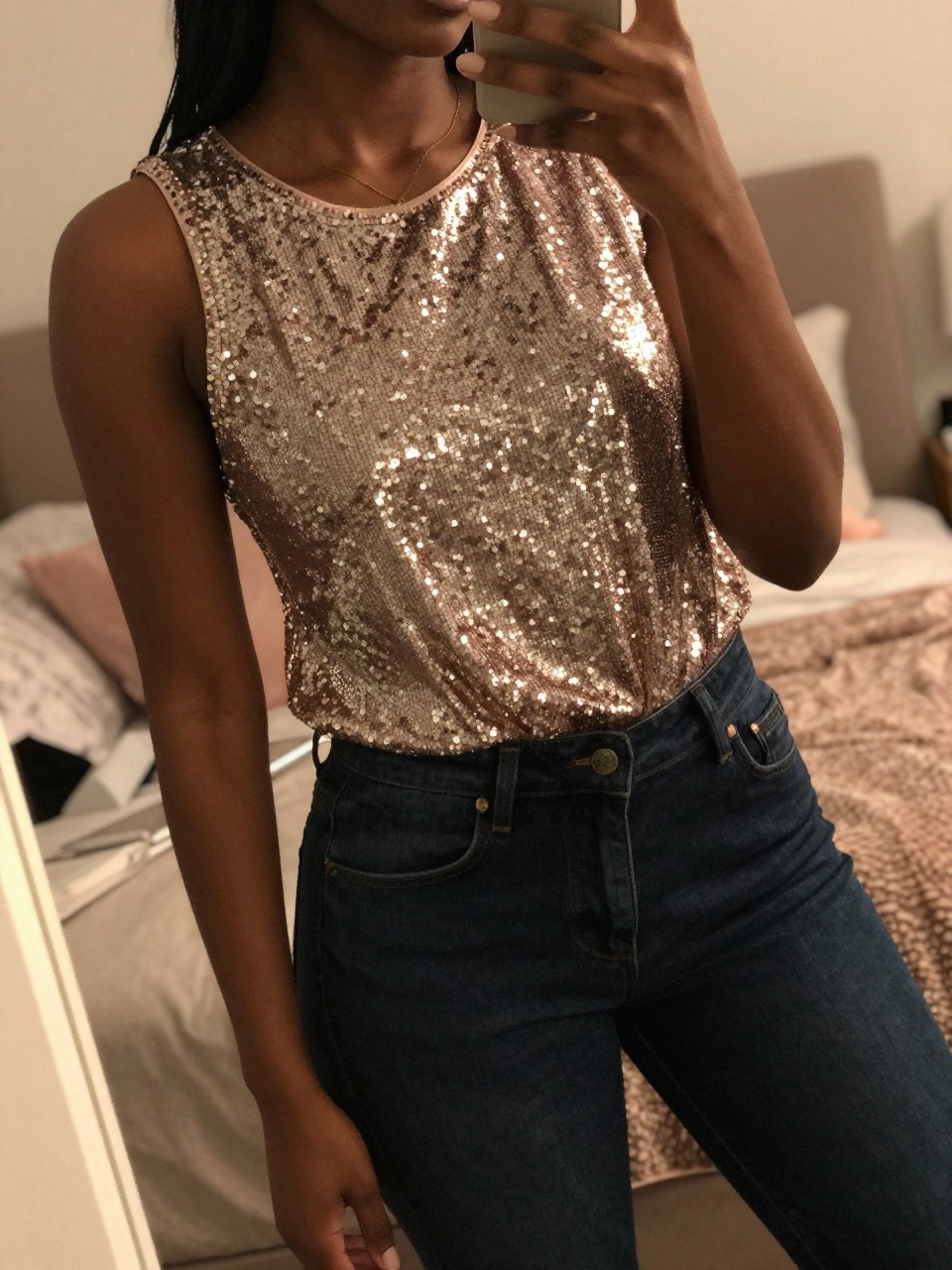 iPhone mirror selfie of a black woman in a sequin top and dark jeans, angled to catch the light on the top, cropped at NECK so face doesn't show, in a feminine-themed bedroom with warm moody lighting, iPhone photo quality.