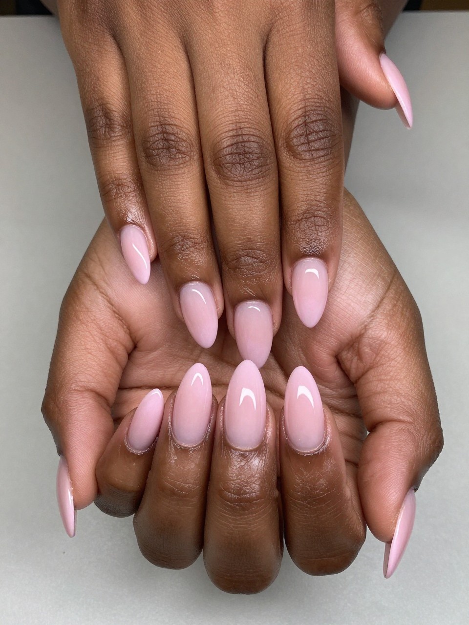 Bird's-eye view of black feminine hands with almond nails. The tips of the nails have a gentle pink ombré fade. The effect is dreamy and romantic.