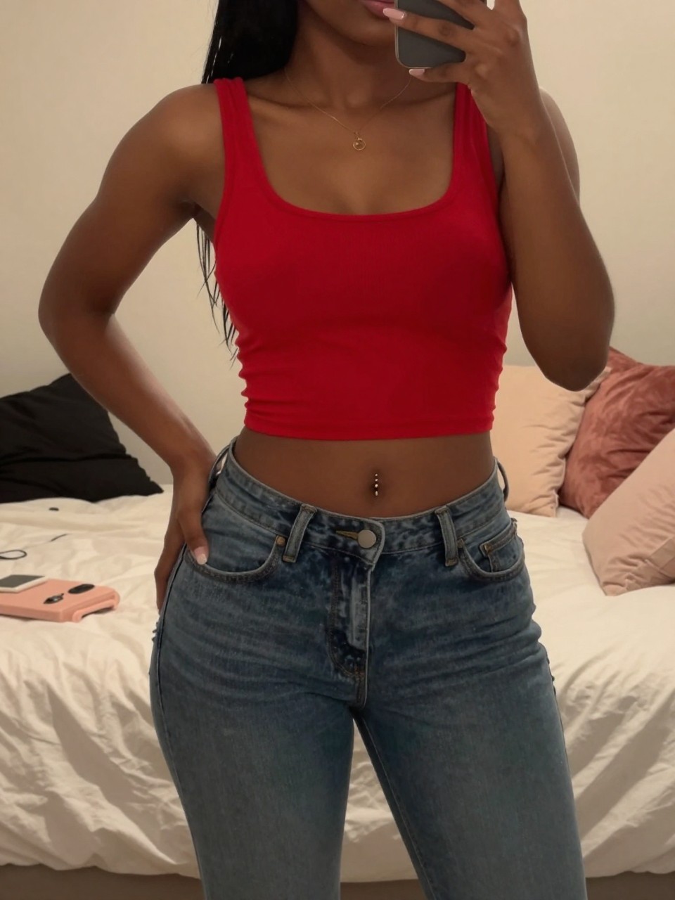 mirror selfie of a black woman in a red crop top and low-rise jeans, hand on hip, cropped at NECK so face doesn't show, in a feminine-themed bedroom with warm moody lighting, iPhone photo quality.