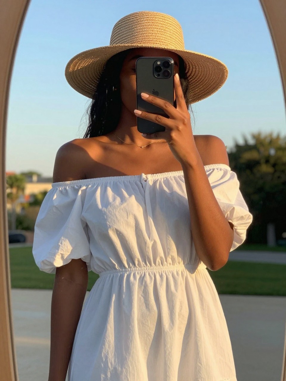 mirror selfie of a black woman in a white off-shoulder dress and straw hat, cropped at NECK so face doesn't show, in a sunny outdoor setting during evening golden hour, iPhone photo quality.
