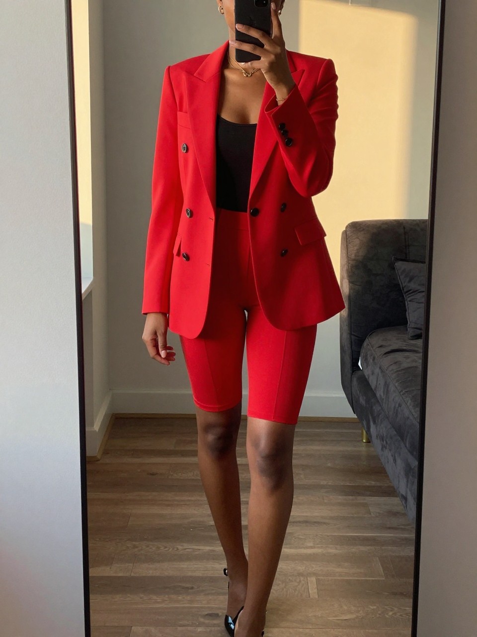 mirror selfie of a black woman in a red blazer and bike shorts, one foot forward, cropped at NECK so face doesn't show, in apartment during evening golden hour, iPhone photo quality.