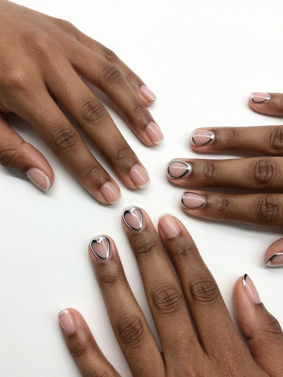 Close-up of black feminine hands with natural, short nails on a white surface. On each nail, a bold, wide outline of a heart is drawn in bright chrome, leaving the inside of the heart clear. The look is minimalist, modern, and strikingly clean.