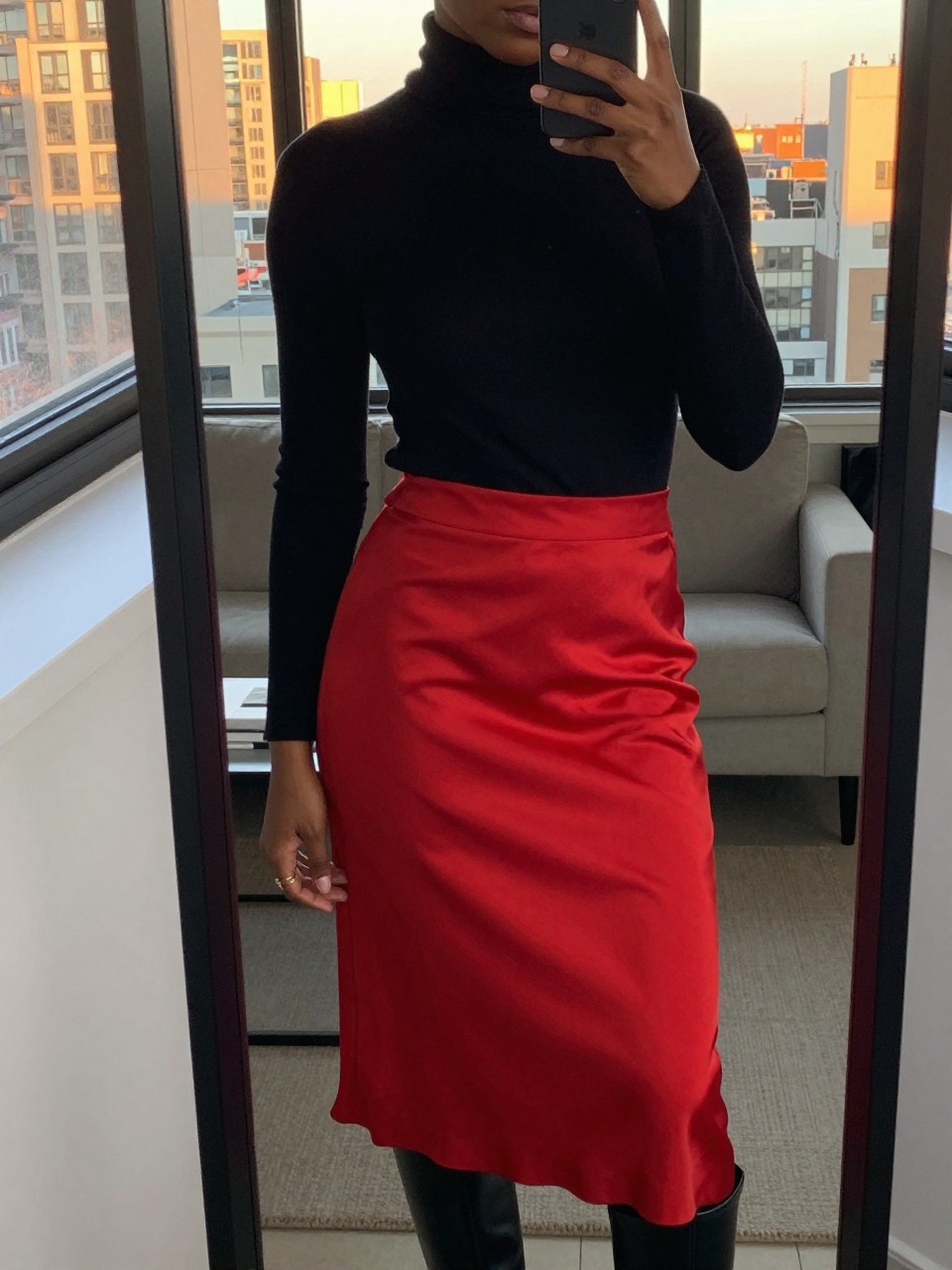 mirror selfie of a black woman in a black turtleneck and red silk skirt with boots, angled slightly, cropped at NECK so face doesn't show, in a city apartment during evening golden hour, iPhone photo quality.