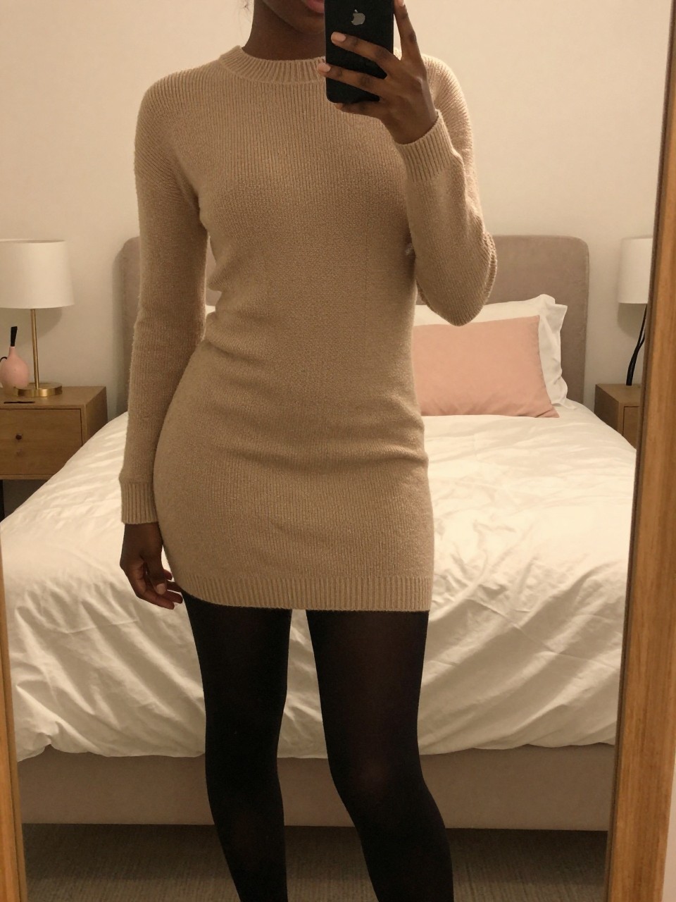 iPhone mirror selfie of a black woman in a sweater dress and tights with Timbs, slight angle, cropped at NECK so face doesn't show, in a feminine-themed bedroom with warm moody lighting, iPhone photo quality.