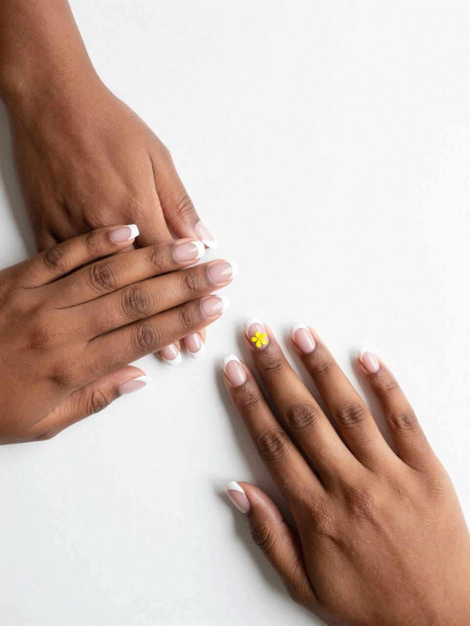 Top-down view of black feminine hands with neat, short nails on a white desk. The nails have a white French tip with a geometric cut-out near the side. A tiny yellow flower is painted inside the negative space. The design is architectural and cute.