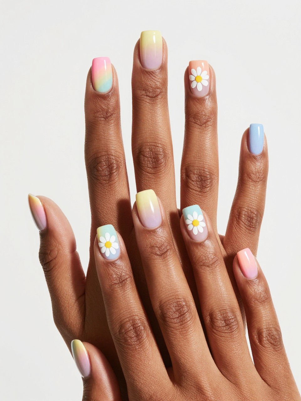 Overhead shot of black feminine hand with short nails, fingers splayed. Each nail has a different pastel rainbow-colored French tips and there is also a white daisy painted on the nails. The effect is cohesive, happy, and bright.