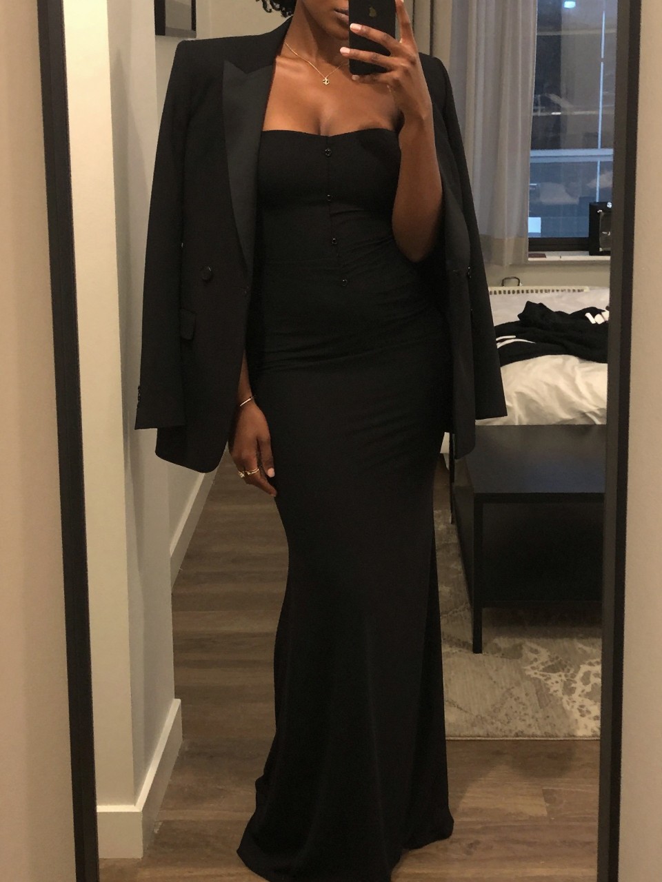 mirror selfie of a black woman in a gown with a blazer draped over her shoulders, looking over shoulder, cropped at NECK so face doesn't show, in a city apartment, warm moody lighting, iPhone photo quality.