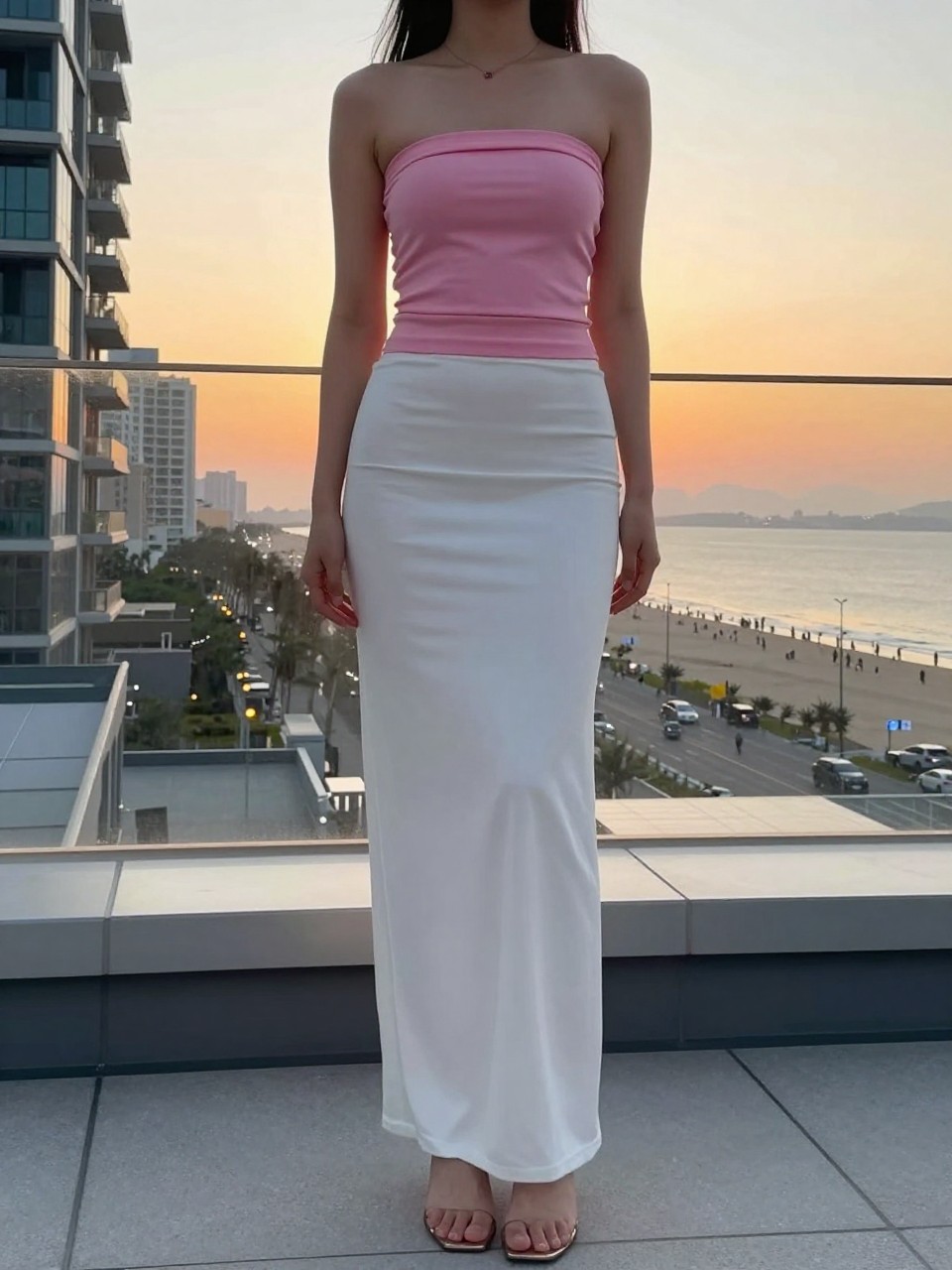 photo of a woman in a pink tube top and white maxi skirt with heels, standing at a sunset beach or rooftop, cropped at NECK so face doesn't show, in a city apartment, evening golden hour, iPhone photo quality.