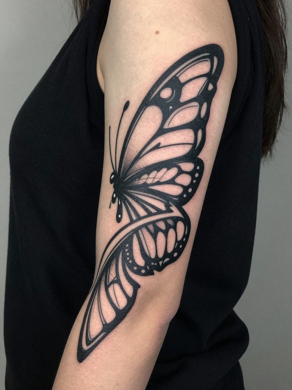 Upper arm wrap tattoo: thick, flowing tribal bands that, upon closer look, form the repeated shape of abstract butterfly wings within the pattern.