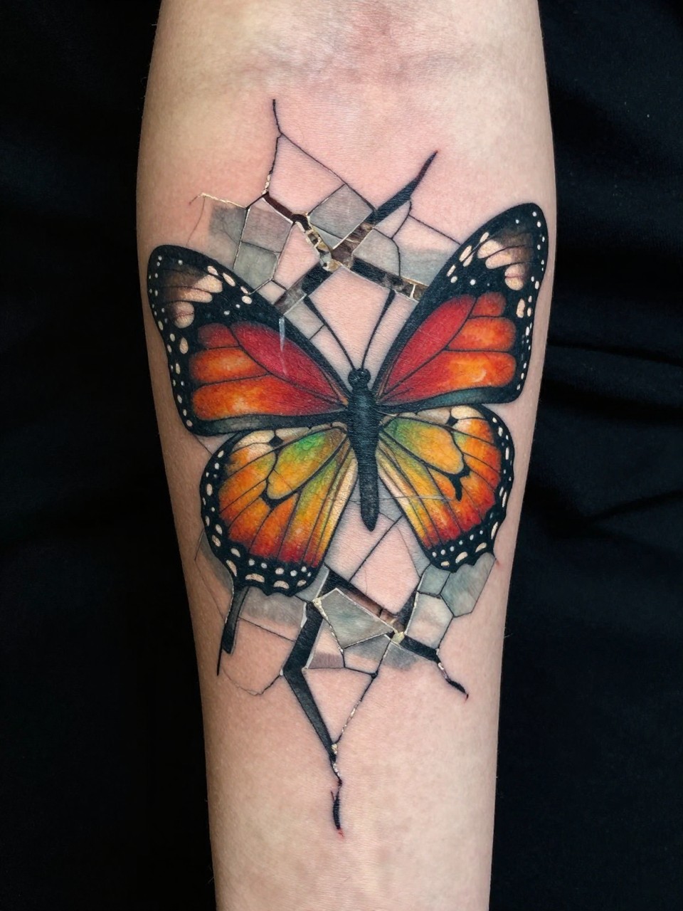 Detailed arm shot tattoo: a mosaic tile pattern cracking apart, with colorful butterfly wings emerging from the fissures. Texture of tile grout and smooth wings contrasted."