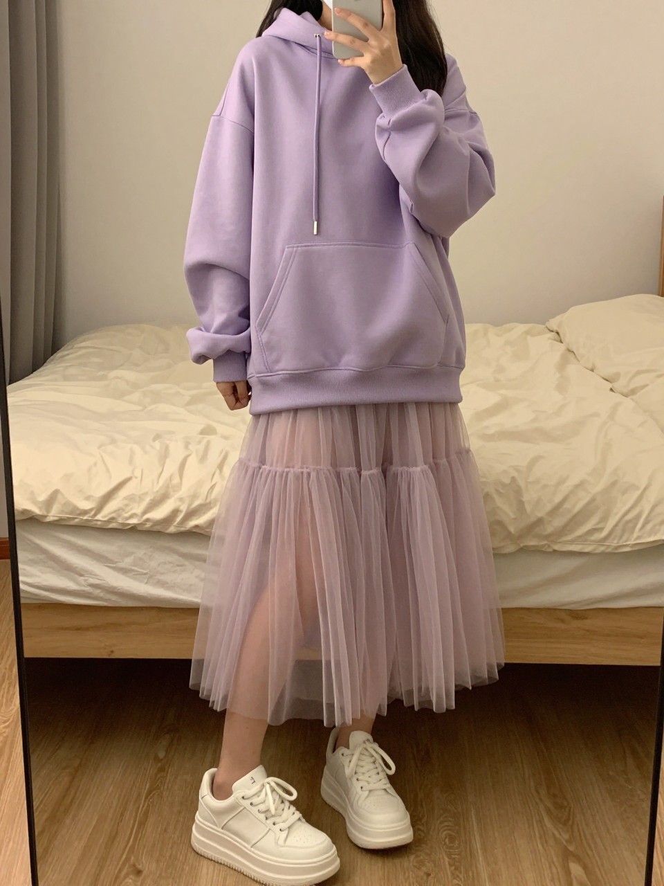 mirror selfie of a woman wearing an oversized lavender hoodie with a layered pastel tulle fairy skirt and chunky white platform sneakers, one hand holding her phone low by her thigh, cropped at NECK so face doesn't show, in a feminine-themed bedroom, warm moody lighting, iPhone photo quality.