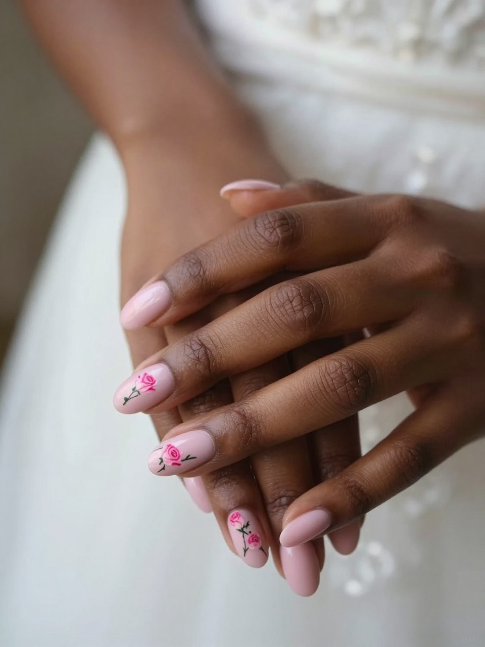 Side-angle view of a black feminine bride’s hand with oval nails. On the oval nail design, vertical line of three small pink rosebuds is on each soft pink nail. The look is cohesive, romantic, and full of gentle movement.