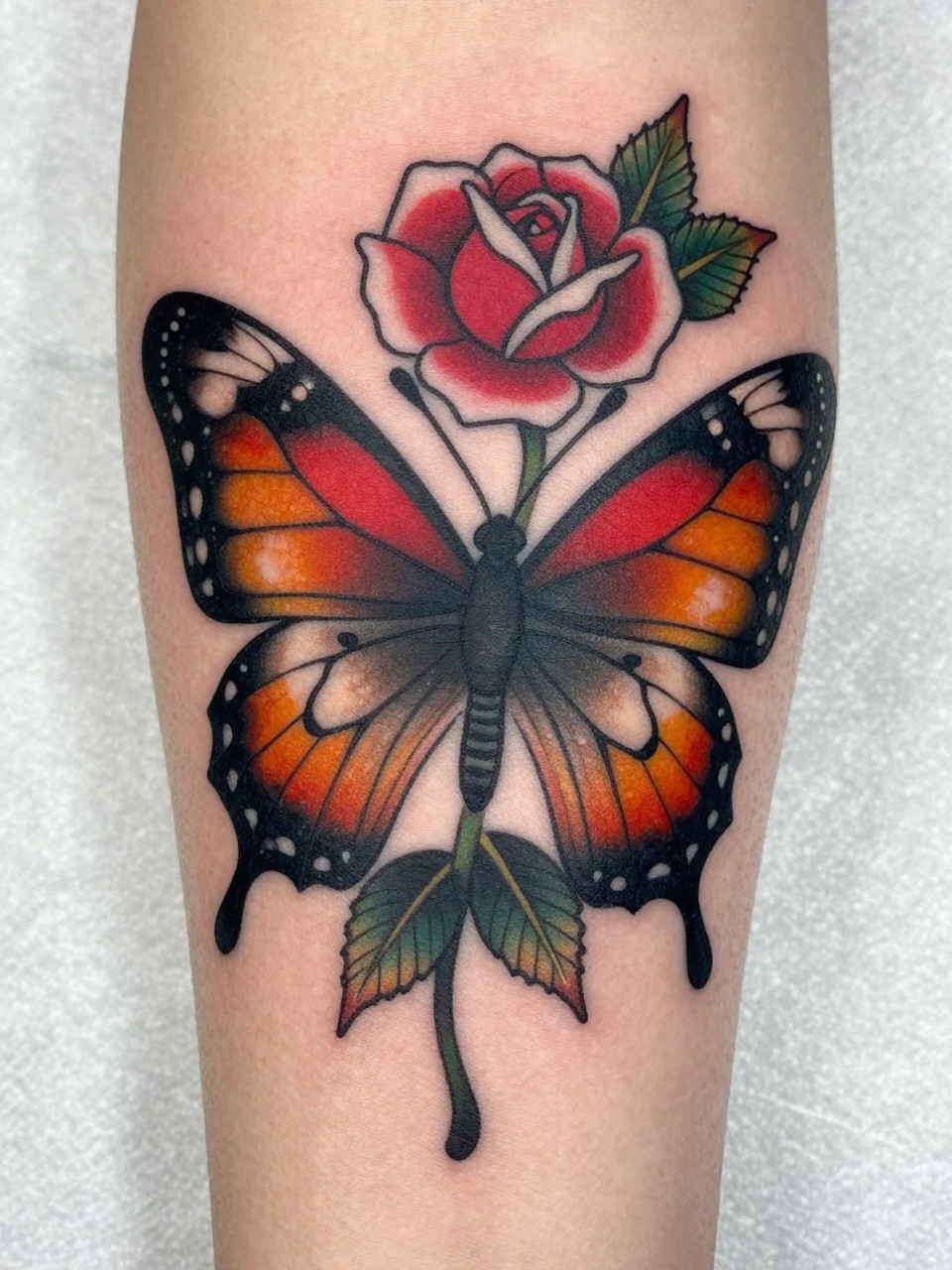 Section of a forearm tattoo: a neo-traditional butterfly with a rose in its mandibles, bold black outlines, and deep color saturation. Rich, illustrative, and cohesive with surrounding scrollwork.