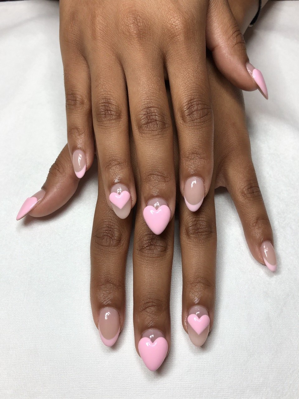 Close-up, top-down view of black feminine hands with a classic French manicure, but the tips are formed into perfect, soft baby pink hearts. Hands rest on a clean, white tablecloth. The look is pristine, elegant, and subtly playful.