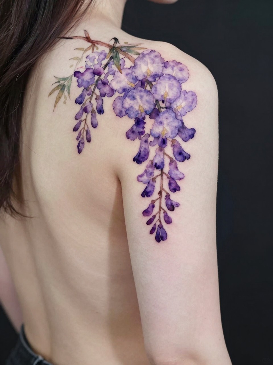 Diagonal back composition tattoo: soft purple and lavender watercolor wisteria clusters trailing from the shoulder down toward the opposite hip. The color bleeds like watercolor paint on paper."