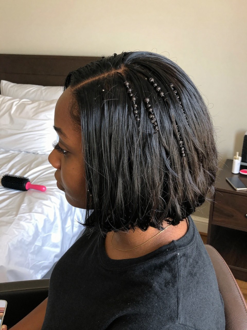 Photo of a black woman wearing a bob set with flexi rods, back-of-head view showing the uniform curl pattern, setting is a bedroom with morning light and a satin pillowcase visible, containing a flexi rod on her nightstand, iPhone photo quality.