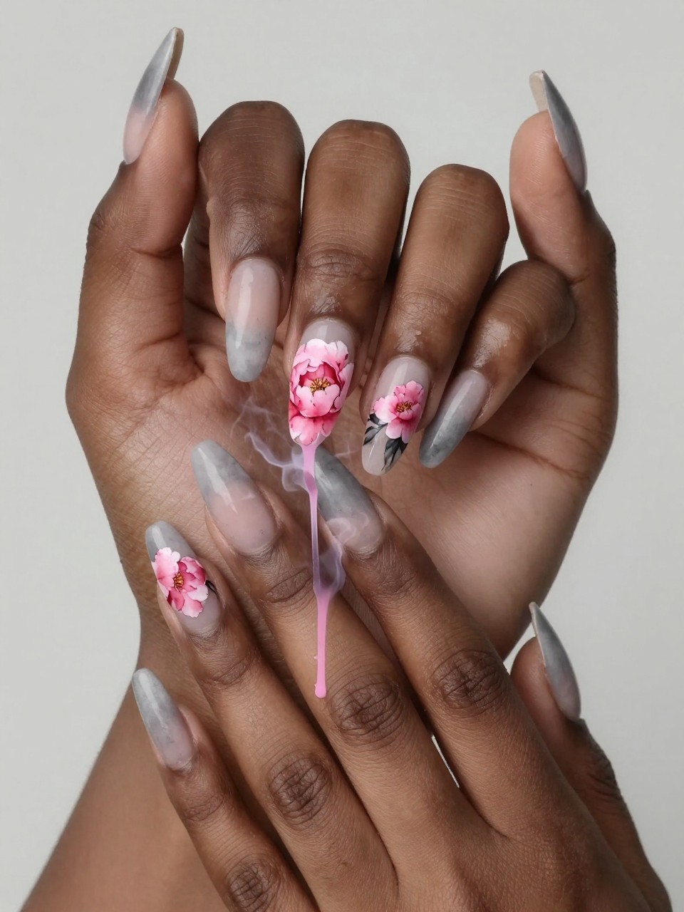 Angled view of black feminine hands with long nails. The tips of the nails have a soft, grey effect. on the nails is also a watercolor-style pink peony shape bleeds from the smoke into the sheer base. The look is dreamy, abstract, and painterly.