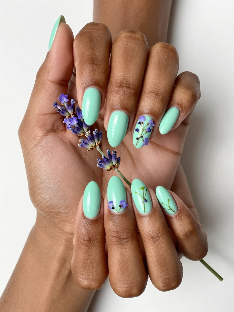 Bird's-eye view of black feminine hands with almond nails gently holding a sprig of lavender. The nails are a glossy mint green. Small clusters of lavender flowers with micro green stems are painted on each nail. The light is bright and clear, like a spring morning.