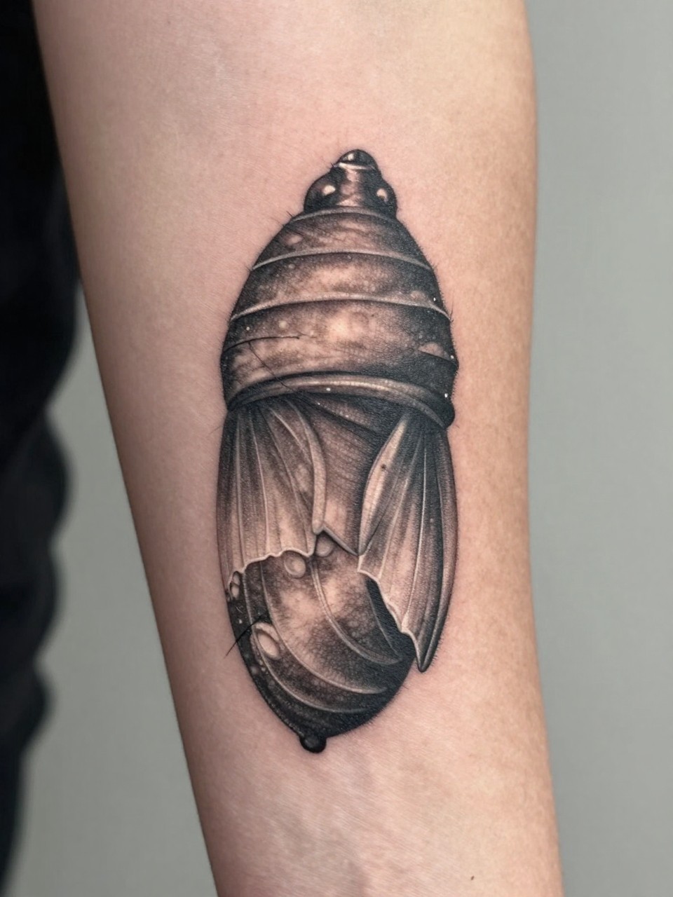 Close-up detail of a forearm sleeve tattoo: a hyper-realistic chrysalis tattoo with fine threads, transitioning into emerging wing tips. Rich textures, focused on the moment of breaking free."
