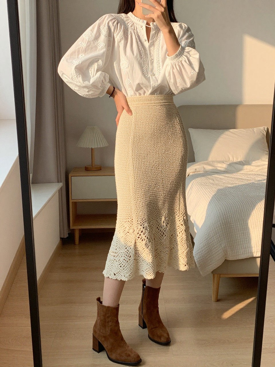 mirror selfie of a woman wearing a white embroidered puff-sleeve blouse tucked into a natural crochet midi skirt with brown suede block-heel ankle boots, one hand on her hip, cropped at NECK so face doesn't show, in a feminine-themed bedroom, evening golden hour, iPhone photo quality.