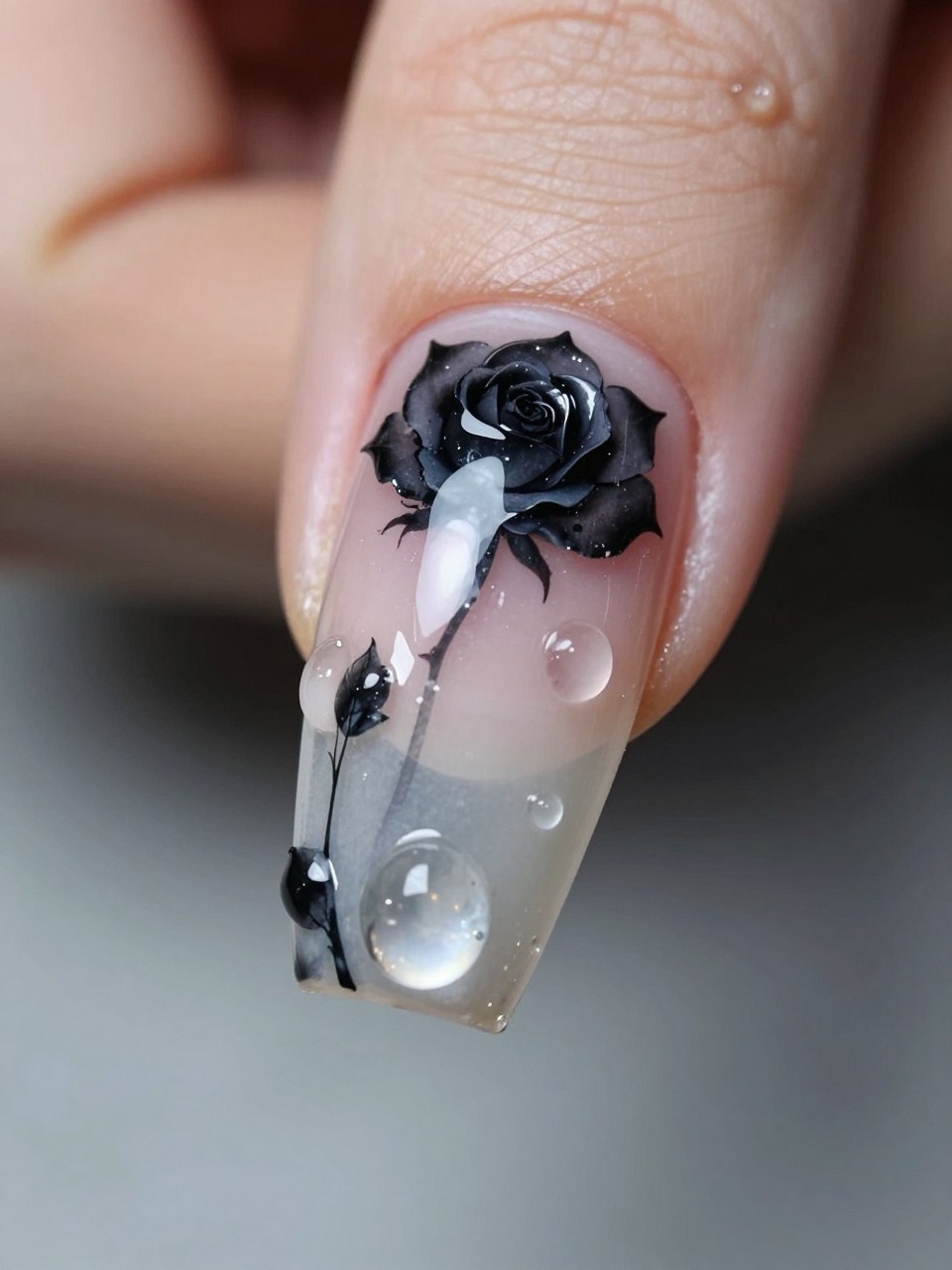 Side-angle macro shot of a long nail. A detailed black rose is painted at the cuticle. Several thick, clear gel droplets in varying sizes are sculpted to look like they're dripping from it down the nail bed. The effect is wet and haunting.