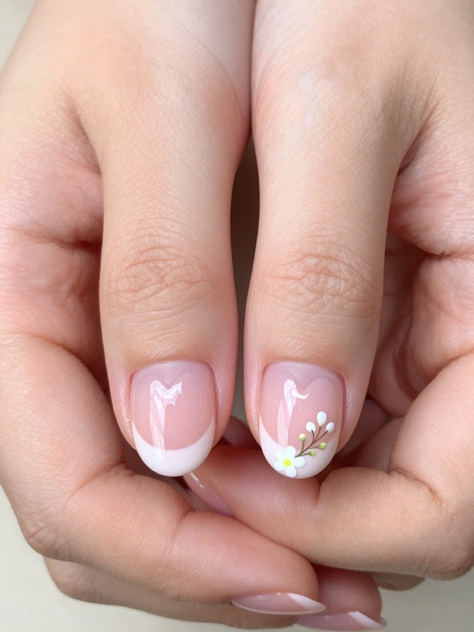Close-up, bird's-eye view of hands with heart-shaped French tips in pale pink. At the base of each heart, where it meets the nail bed, a micro white flower sprig is painted. The look is delicate, feminine, and whimsical.