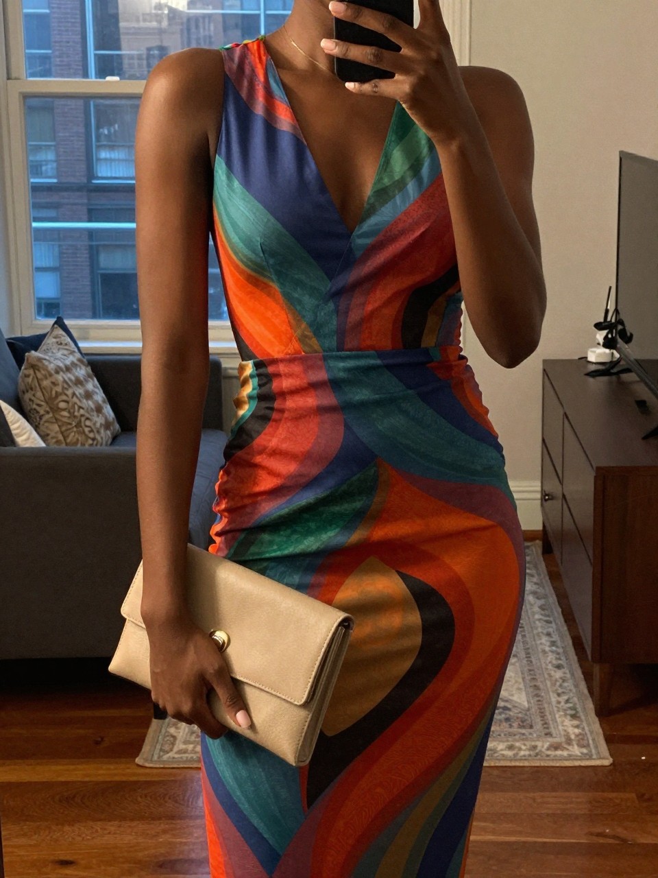 mirror selfie of a black woman in a vibrant colored dress, holding a neutral clutch, cropped at NECK so face doesn't show, in a city apartment, warm moody lighting, iPhone photo quality.