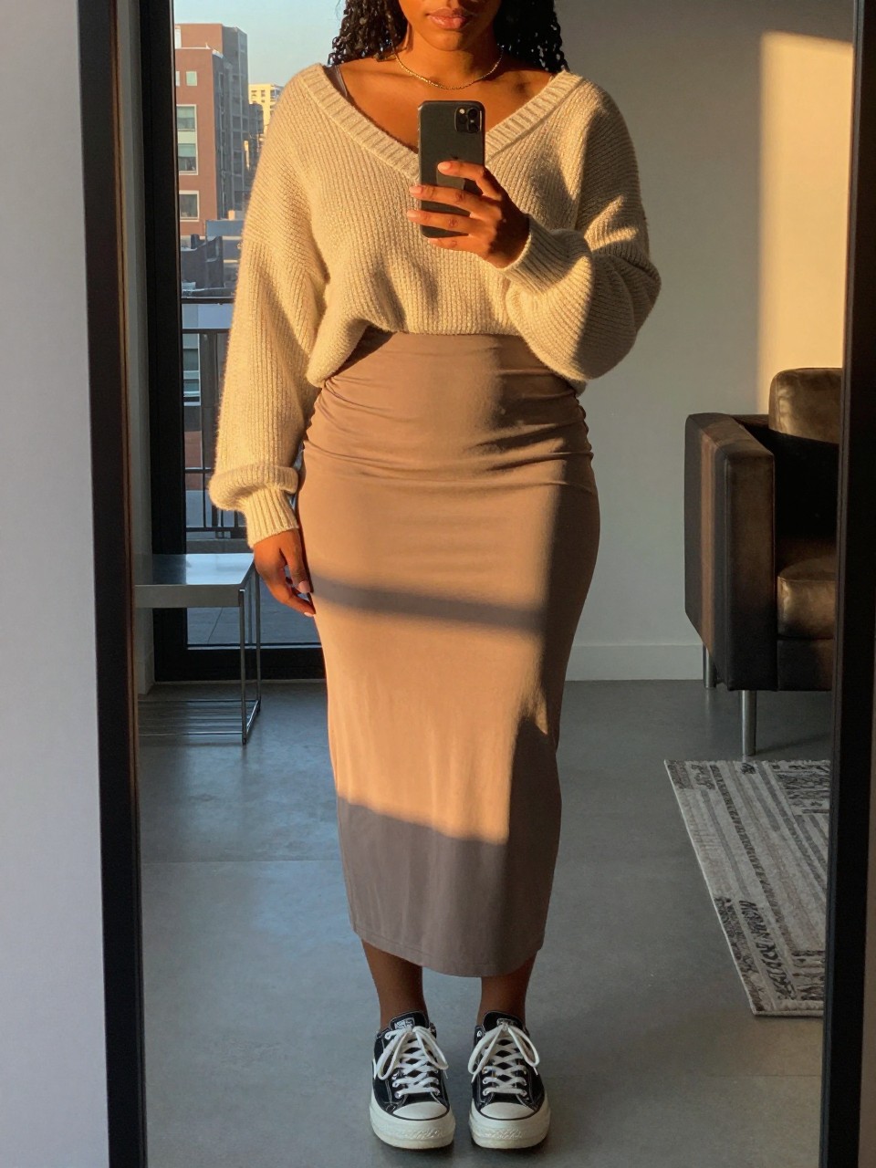 mirror selfie of a curvy black woman in a slip skirt and oversized sweater with sneakers, holding phone at waist, cropped at NECK so face doesn't show, in a city apartment, evening golden hour, iPhone photo quality.