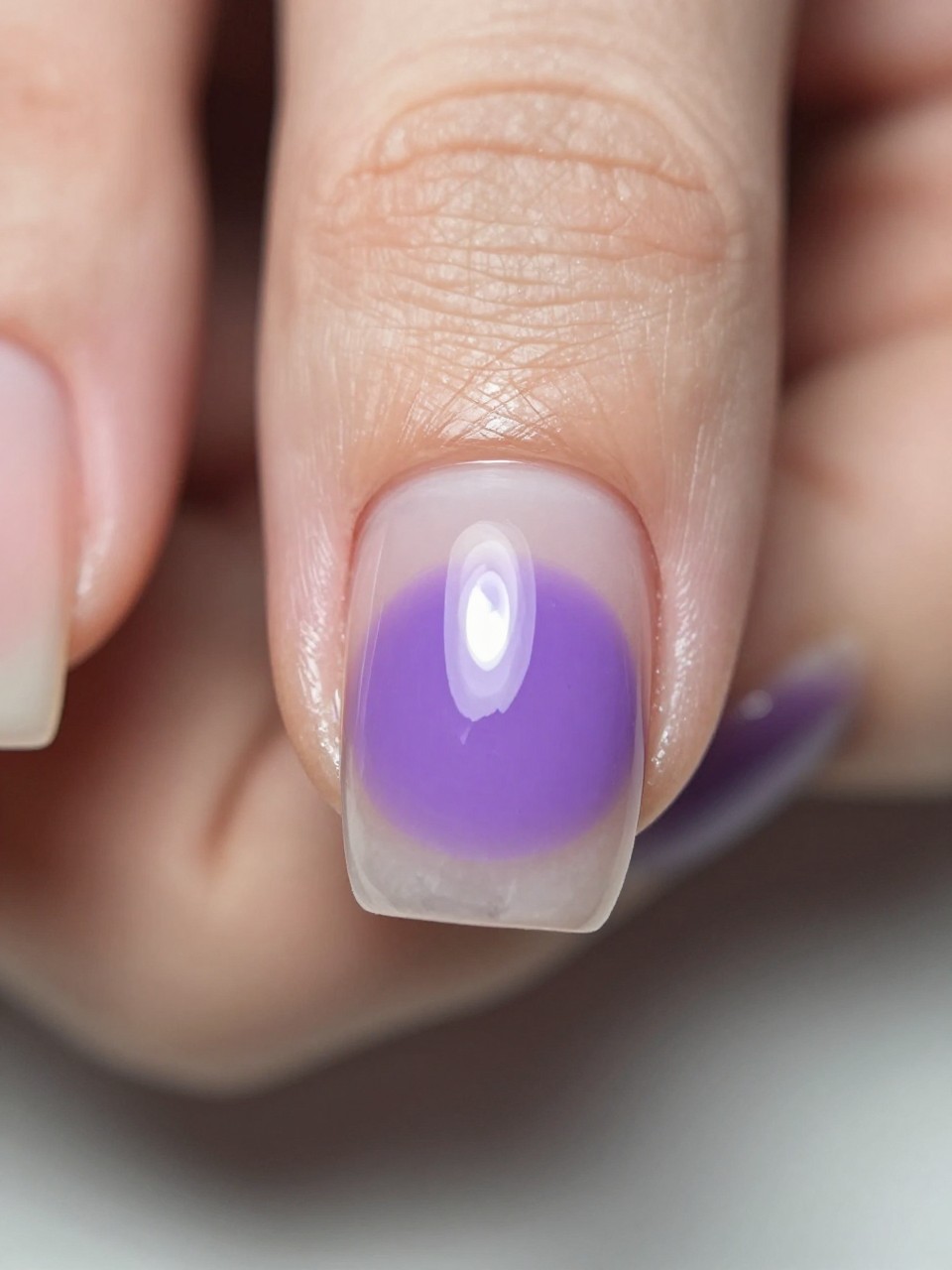 Macro focus on one accent nail. The nail is clear gloss. A single, real pressed violet is perfectly centered and preserved under the gel. The other nails are bare. The detail is exquisite and conversation-starting.