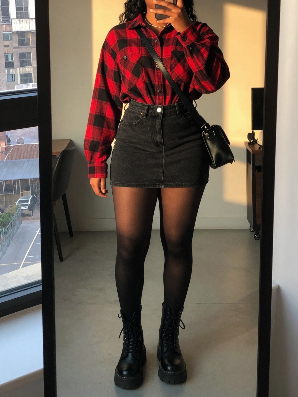 mirror selfie of a black curvy woman wearing a red and black plaid flannel shirt tucked into a black denim mini skirt with black tights and black chunky combat boots, holding a black crossbody bag, standing in a grunge-inspired pose, cropped at NECK so face doesn't show, in a city apartment, evening golden hour, iPhone photo quality.