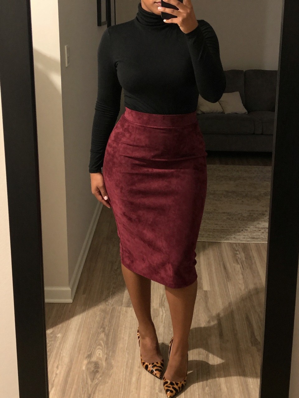 mirror selfie of a curvy black woman wearing a black turtleneck tucked into a maroon suede pencil skirt with animal print heels, standing with her weight shifted to one side, cropped at NECK so face doesn't show, in a city apartment, warm moody lighting, iPhone photo quality.