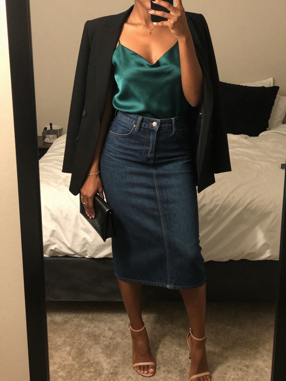 mirror selfie of a black woman wearing an emerald silk camisole tucked into a dark-wash denim midi skirt with a black blazer draped over her shoulders and nude strappy heels, holding a small black clutch, standing in a confident evening pose, cropped at NECK so face doesn't show, in a feminine-themed bedroom, warm moody lighting, iPhone photo quality.