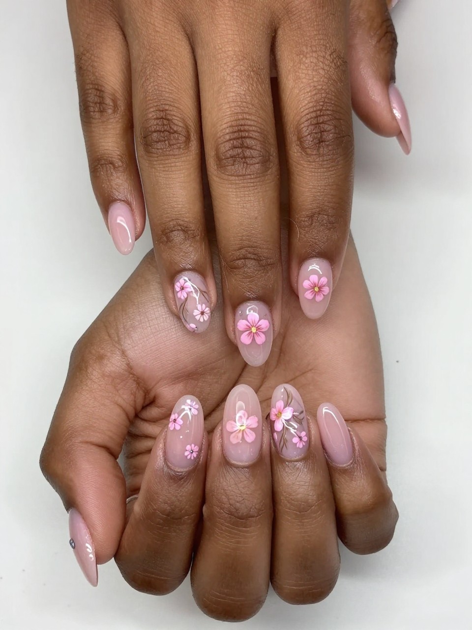 Top-down view of black feminime hands with sheer pink nails, fingers gently splayed. Each nail features a different micro floral design in the same color palette. The overall look is cohesive, intricate, and thoughtfully mismatched.