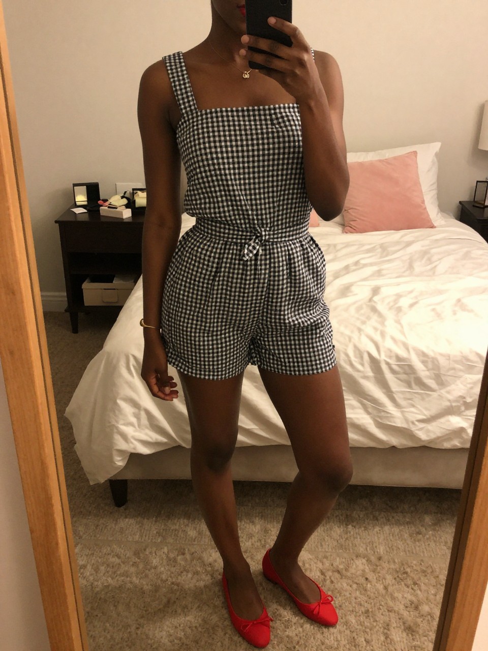 mirror selfie of a black woman in a gingham set and red flats, applying red lipstick, cropped at NECK so face doesn't show, in a feminine-themed bedroom, warm moody lighting, iPhone photo quality.