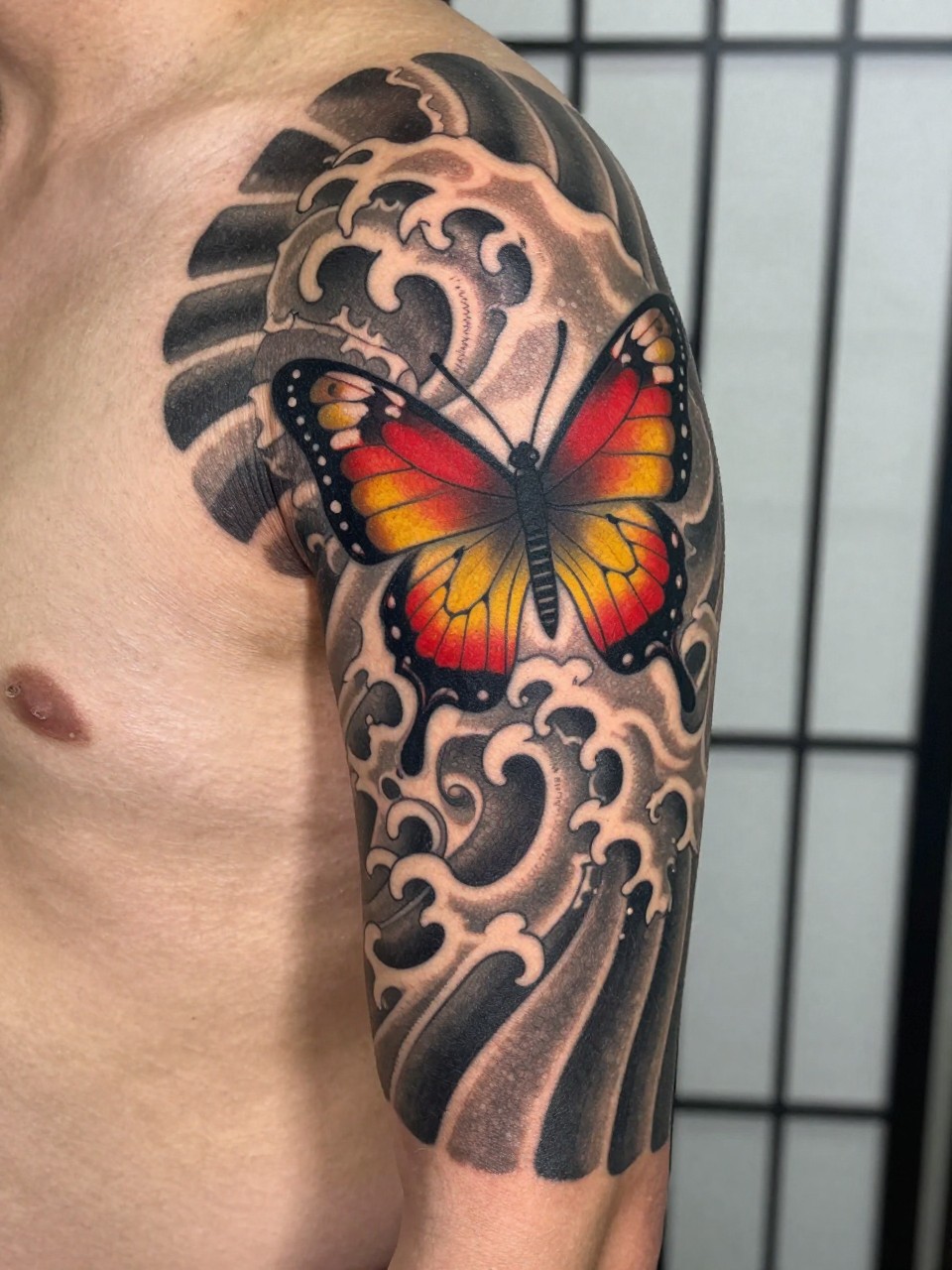 Section of a sleeve in Japanese style tattoo: a bold butterfly with flowing antennae next to crashing wave details. Rich color palette of red, grey, and yellow, following traditional motifs.