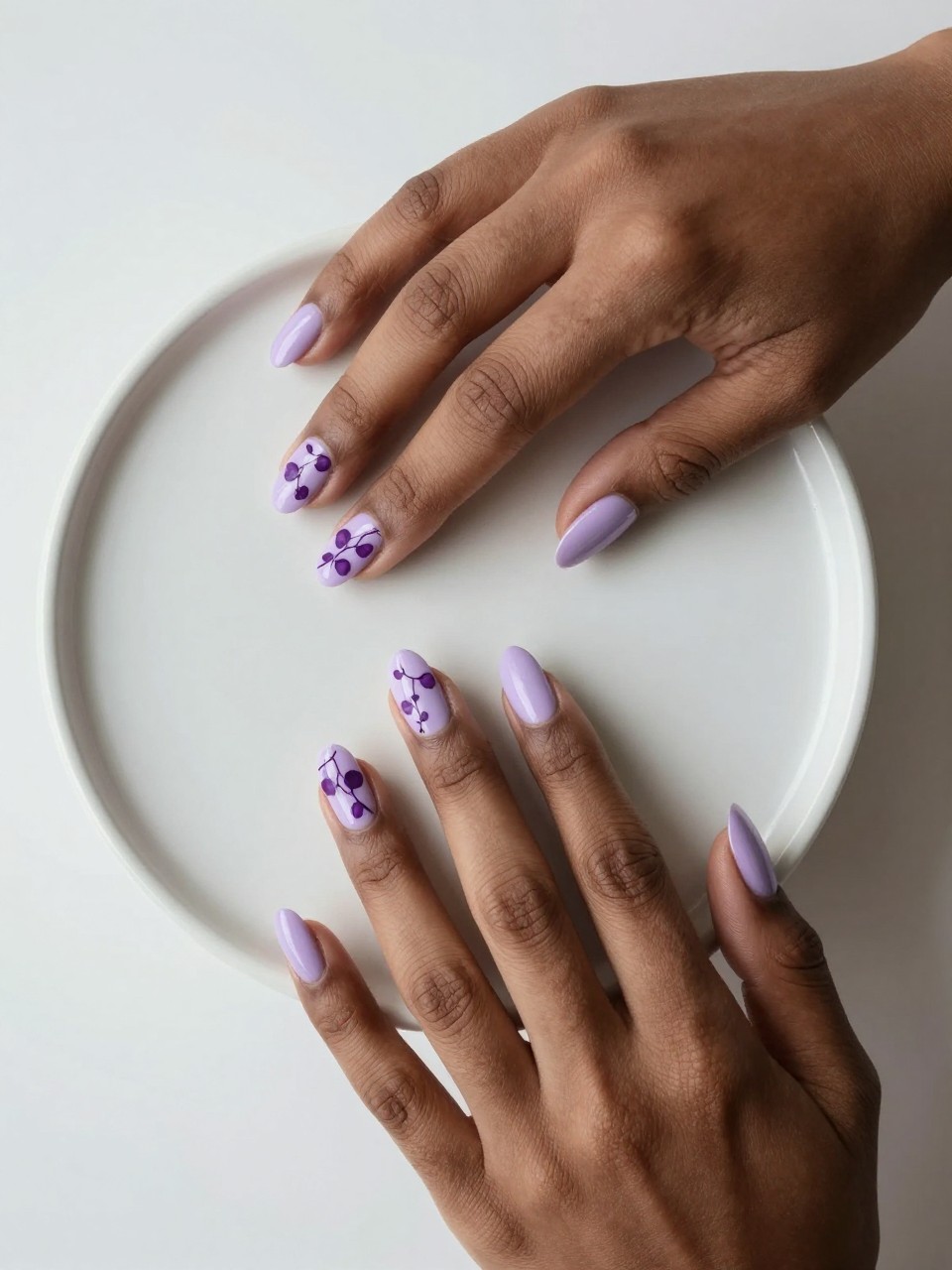 Overhead shot of blcak feminine hands on a minimalist ceramic pot. The nails are pale lavender. A single, fine dark purple vine with tiny heart-shaped leaves trails across each nail. The design is graceful, natural, and softly romantic.