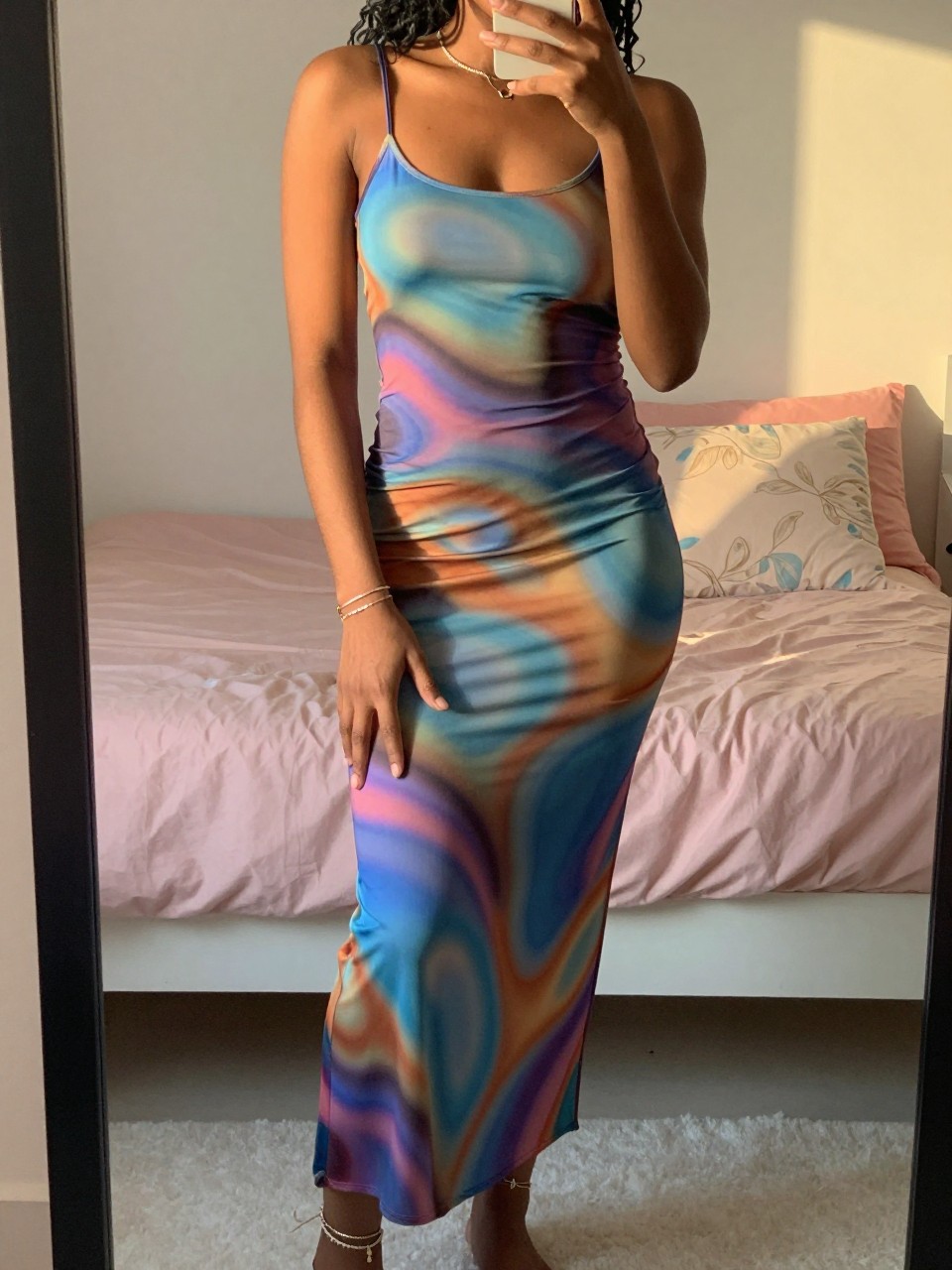 mirror selfie of a black woman in a psychedelic maxi dress, pointing a toe to show anklets, cropped at NECK so face doesn't show, in a feminine-themed bedroom, evening golden hour, iPhone photo quality.