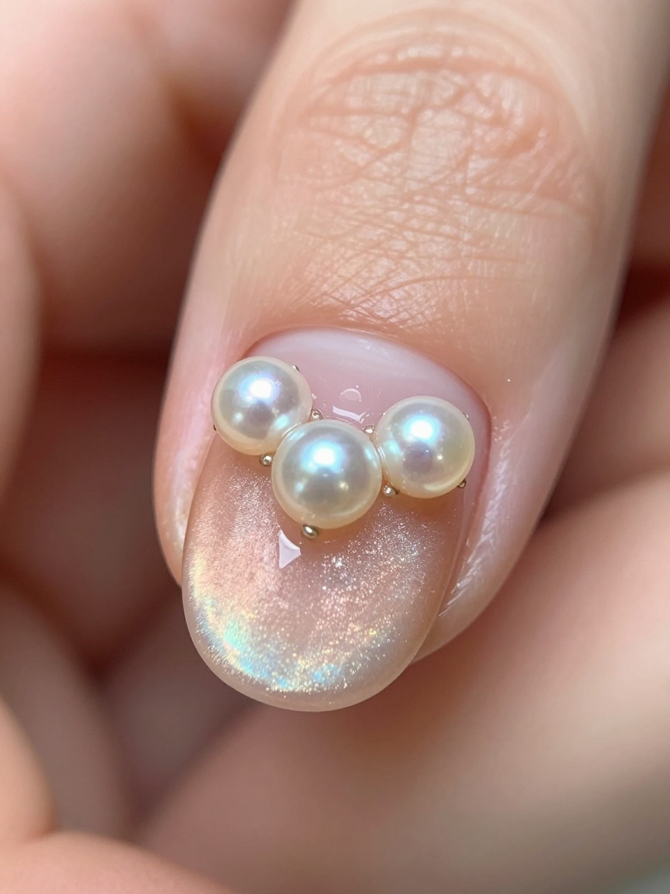 Macro focus on a ring finger nail. The base is a soft peach cat eye. Three micro pearls are arranged in a heart shape near the cuticle. The lighting is soft, highlighting the pearls' texture against the shimmer.