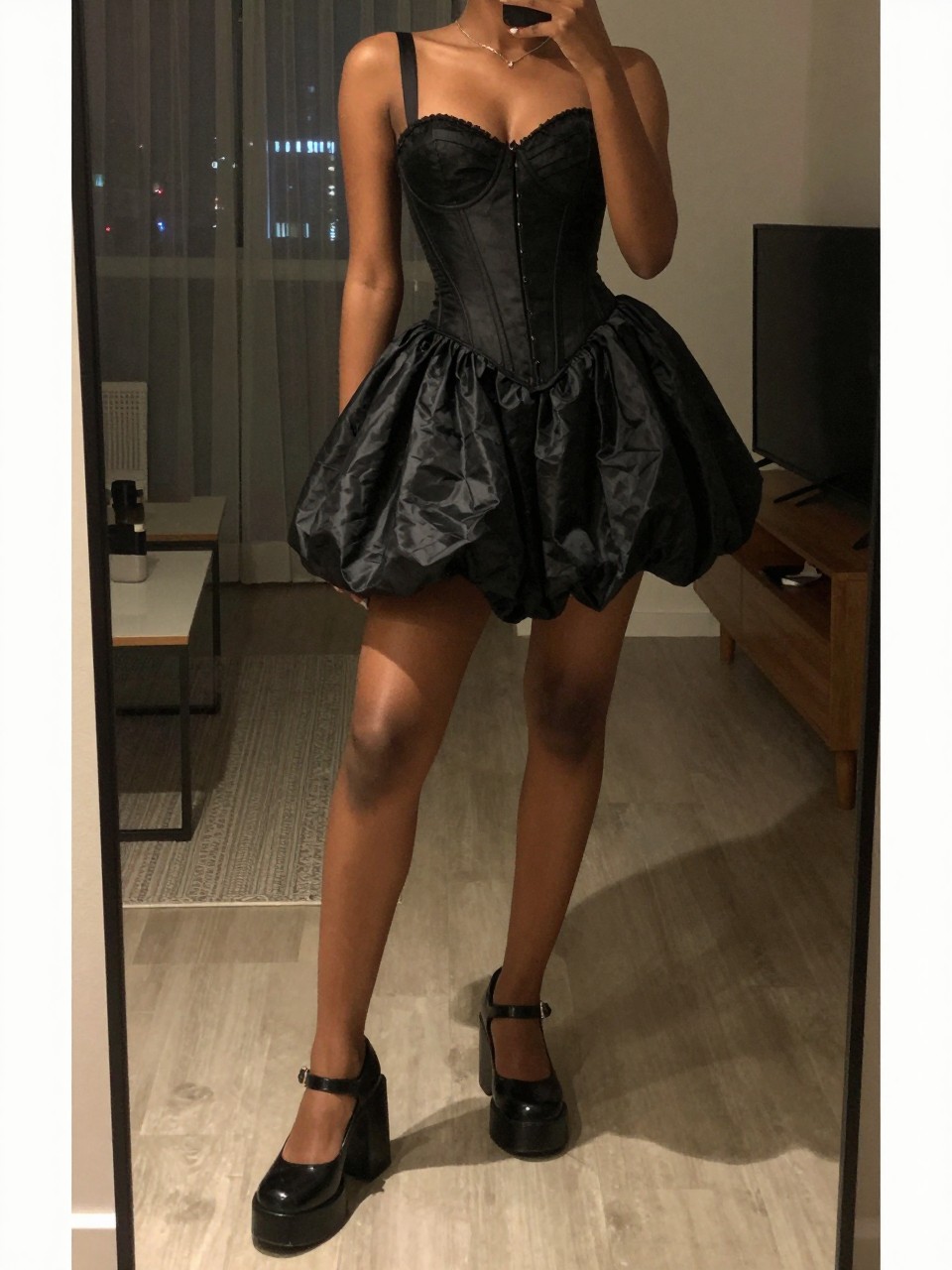 iPhone mirror selfie of a black woman in a black corset top and a black taffeta bubble skirt with chunky Mary Janes, posing with one foot forward, cropped at NECK so face doesn't show, in a city apartment, warm moody lighting, iPhone photo quality.
