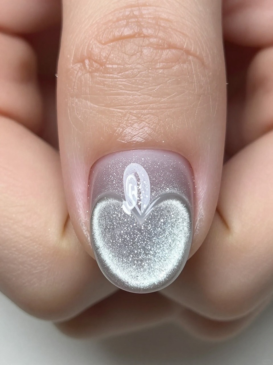 Close-up, top-down view focusing on the nail design. Two distinct lines of silver cat eye glitter run up the nail, meeting at the base to form the bottom of a heart shape. The design is precise and modern.
