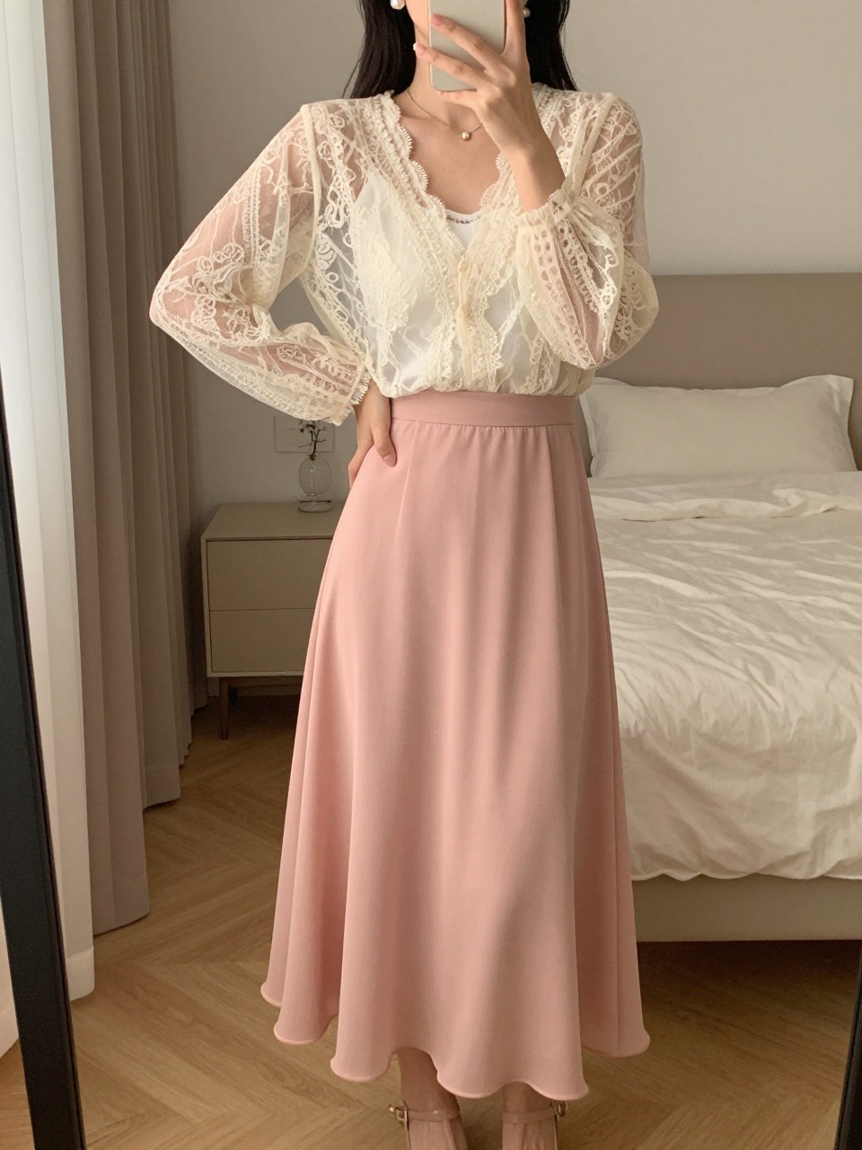 mirror selfie of a woman wearing a sheer cream lace blouse over a white camisole tucked into a blush pink chiffon maxi skirt with nude heeled sandals and pearl stud earrings, standing in a dreamy romantic pose, cropped at NECK so face doesn't show, in a feminine-themed bedroom, warm moody lighting, iPhone photo quality.