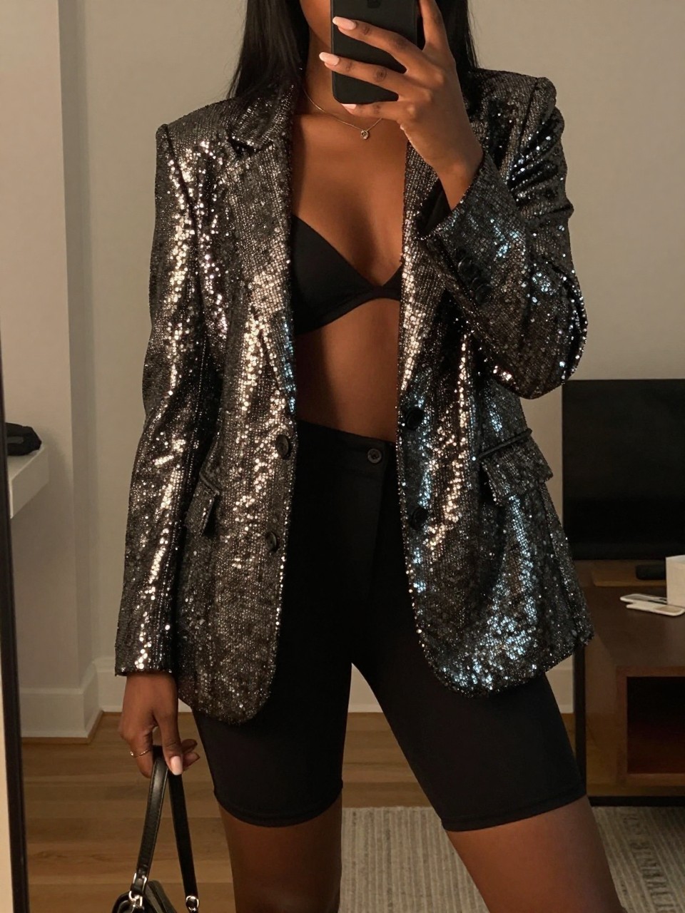 mirror selfie of a black woman in a sequined blazer and biker shorts, blazer worn open, cropped at NECK so face doesn't show, in a city apartment, warm moody lighting, iPhone photo quality.